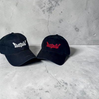 Two black baseball caps with embroidered logos on a concrete surface.