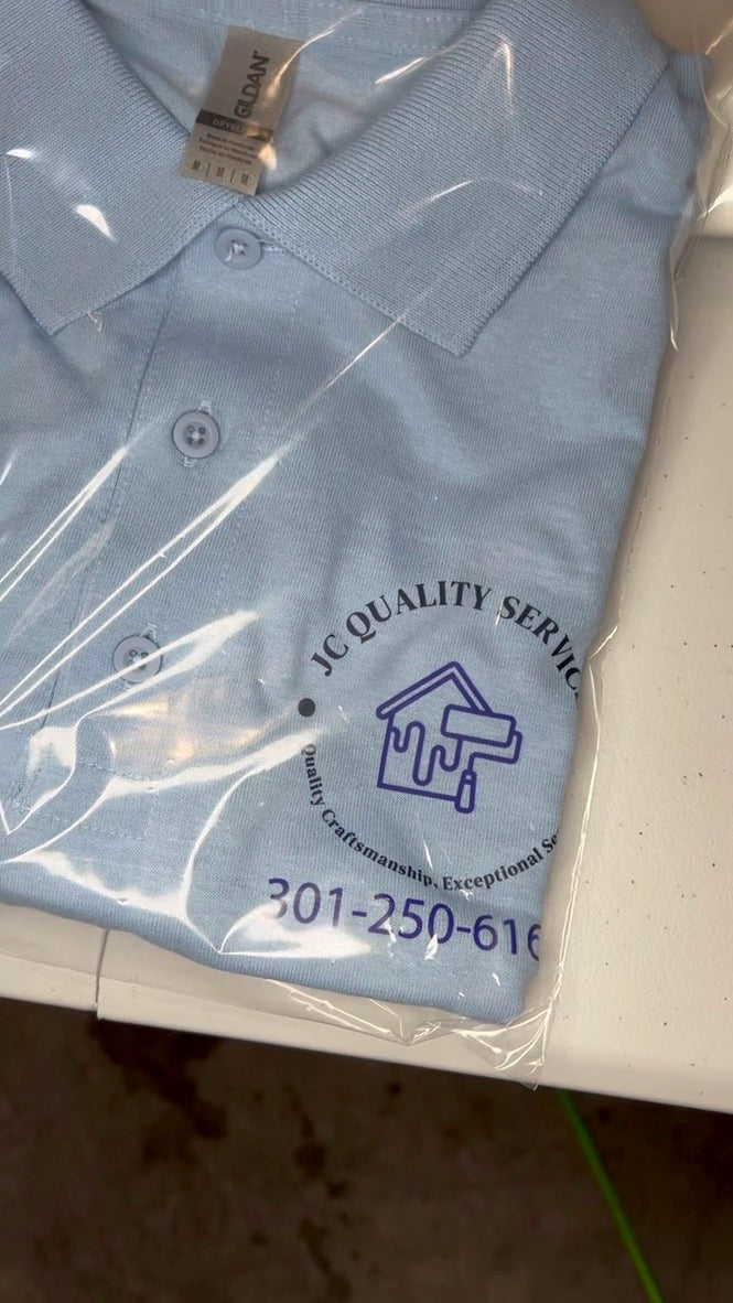 Blue polo shirt with 'JC Quality Service' branding on a white surface