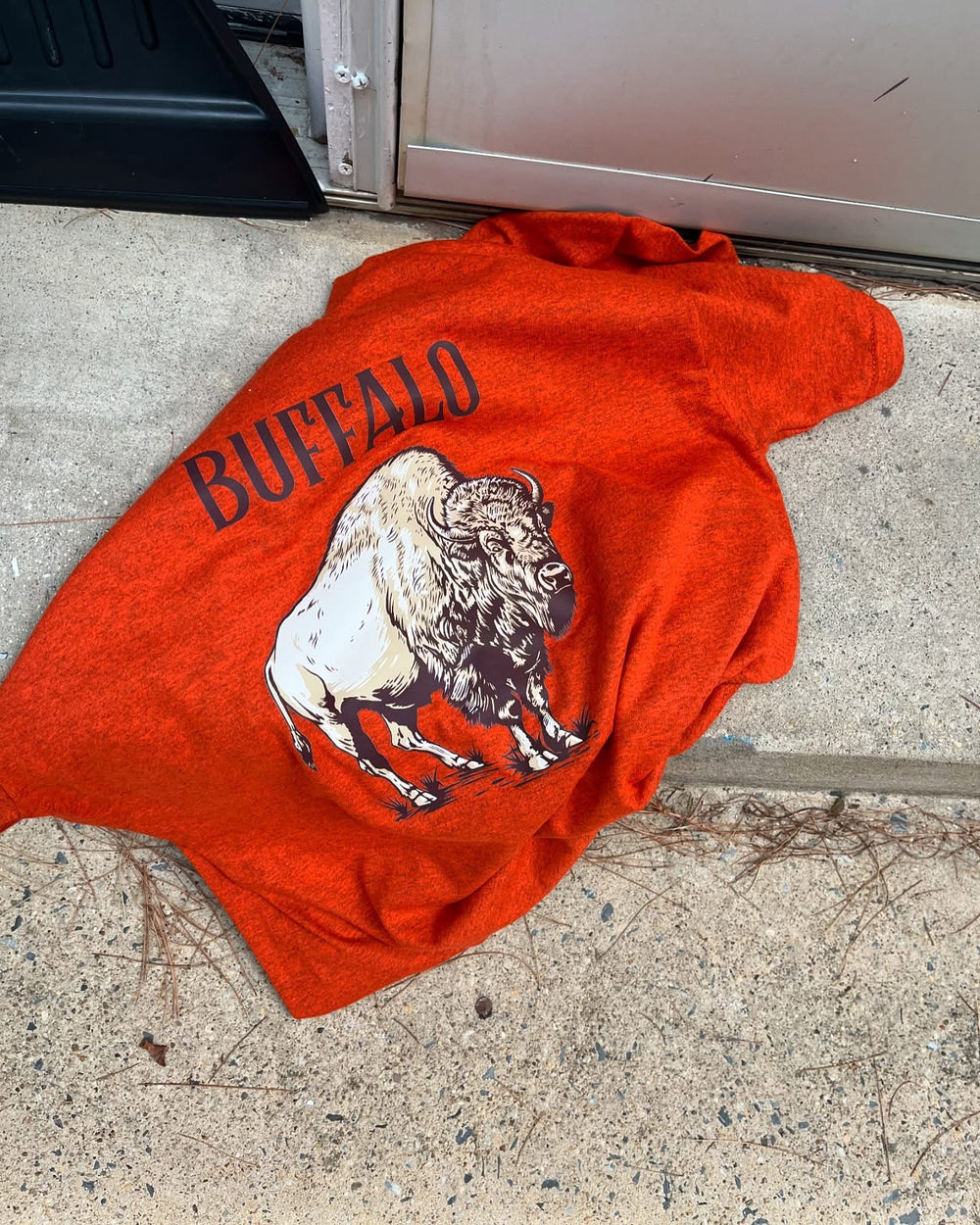 Red shirt with a graphic of a buffalo and the word 'Buffalo' on a concrete floor.