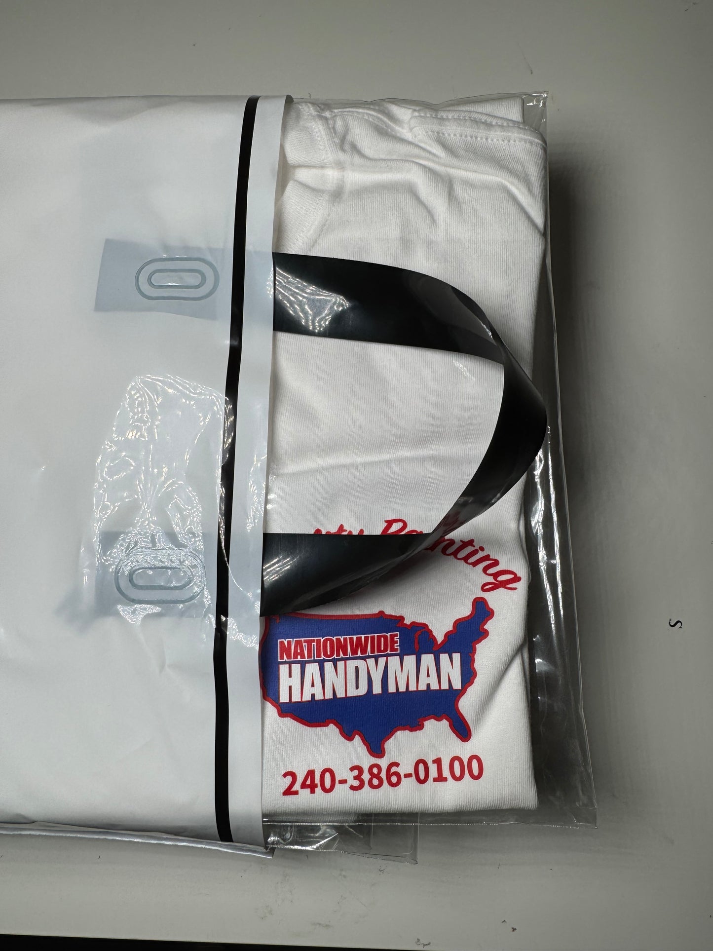 White t-shirt with red and blue graphics in a clear plastic bag on a gray background