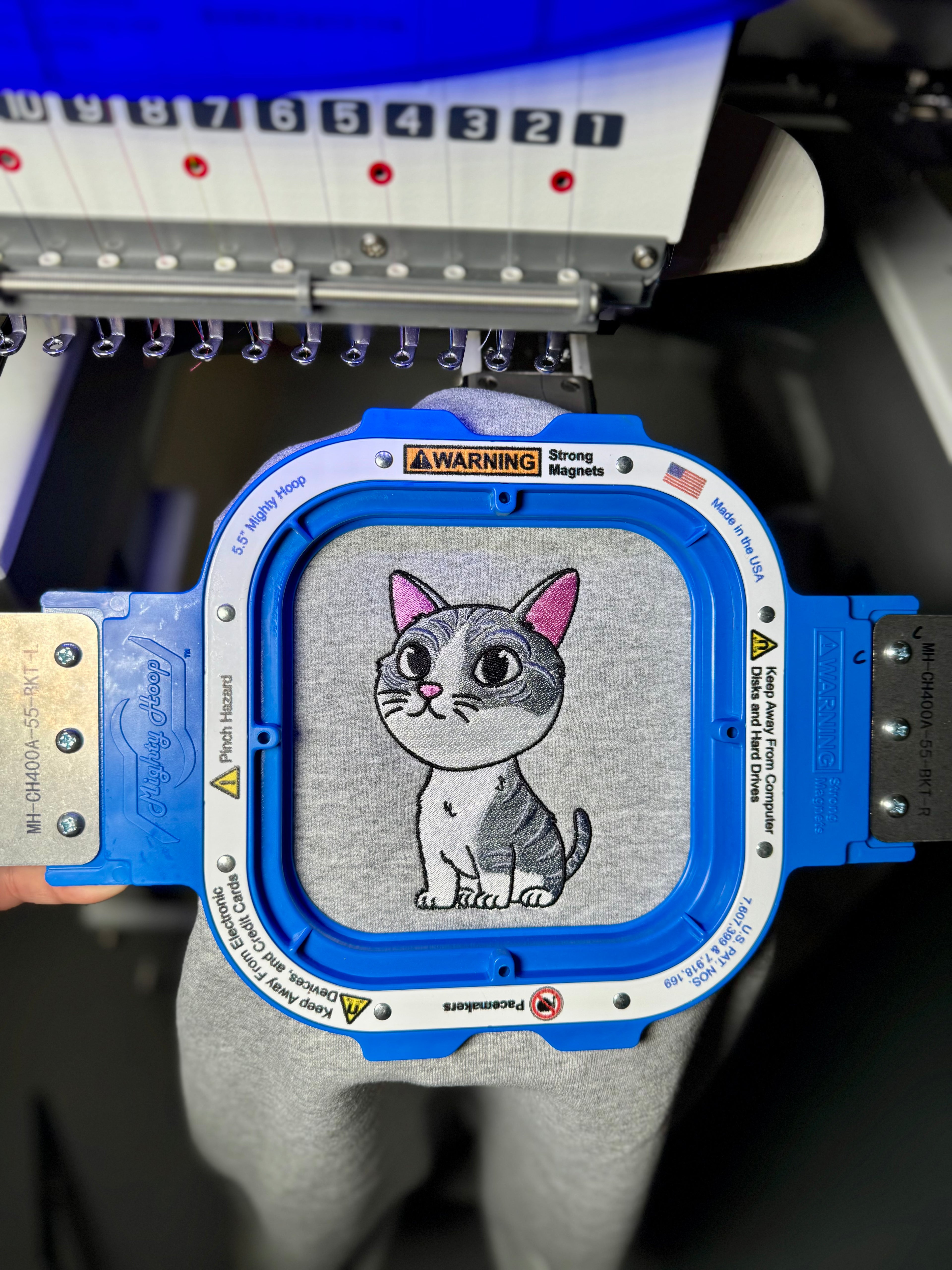 Embroidery machine with a cartoon cat design on a gray fabric