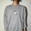 Person wearing a gray sweatshirt with a cat graphic and a black cap against a white wall.