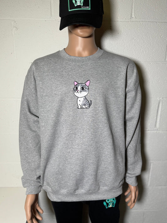 Person wearing a gray sweatshirt with a cat graphic and a black cap against a white wall.