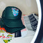 Green cap with colorful design on a white surface with visible brand names.