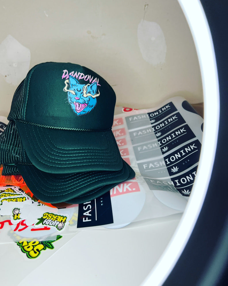 Green cap with colorful design on a white surface with visible brand names.