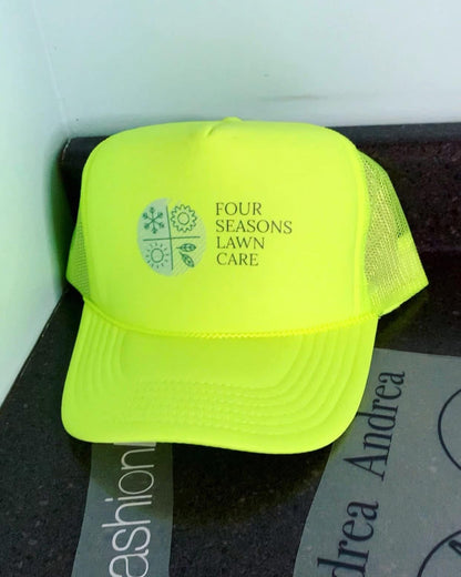 Neon yellow cap with 'Four Seasons Lawn Care' text on a dark surface