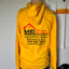 Yellow hoodie with a business logo and contact information on a mannequin against a white wall.
