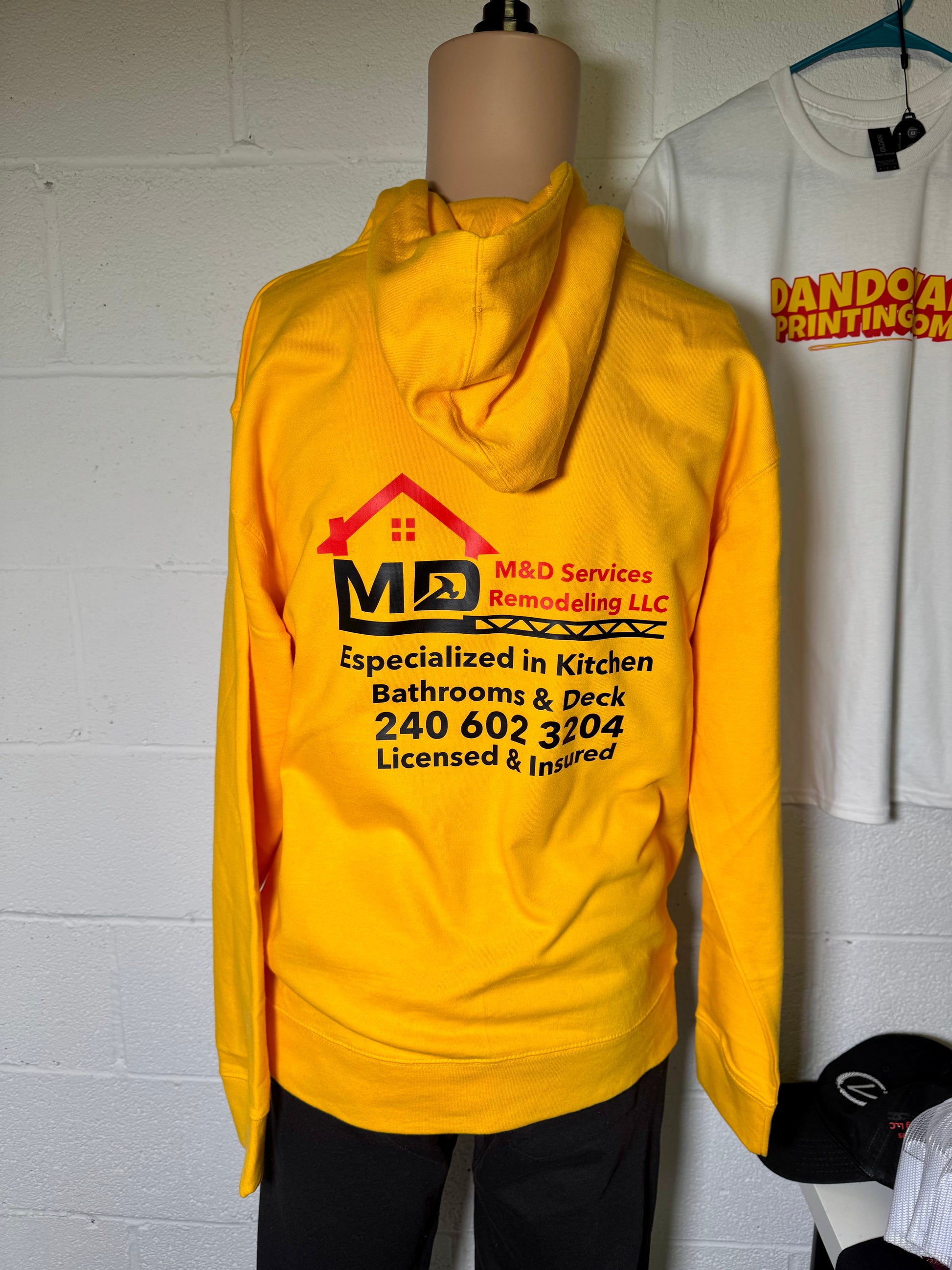 Yellow hoodie with a business logo and contact information on a mannequin against a white wall.