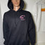 Person wearing a black hoodie with a pink logo on a white floor.