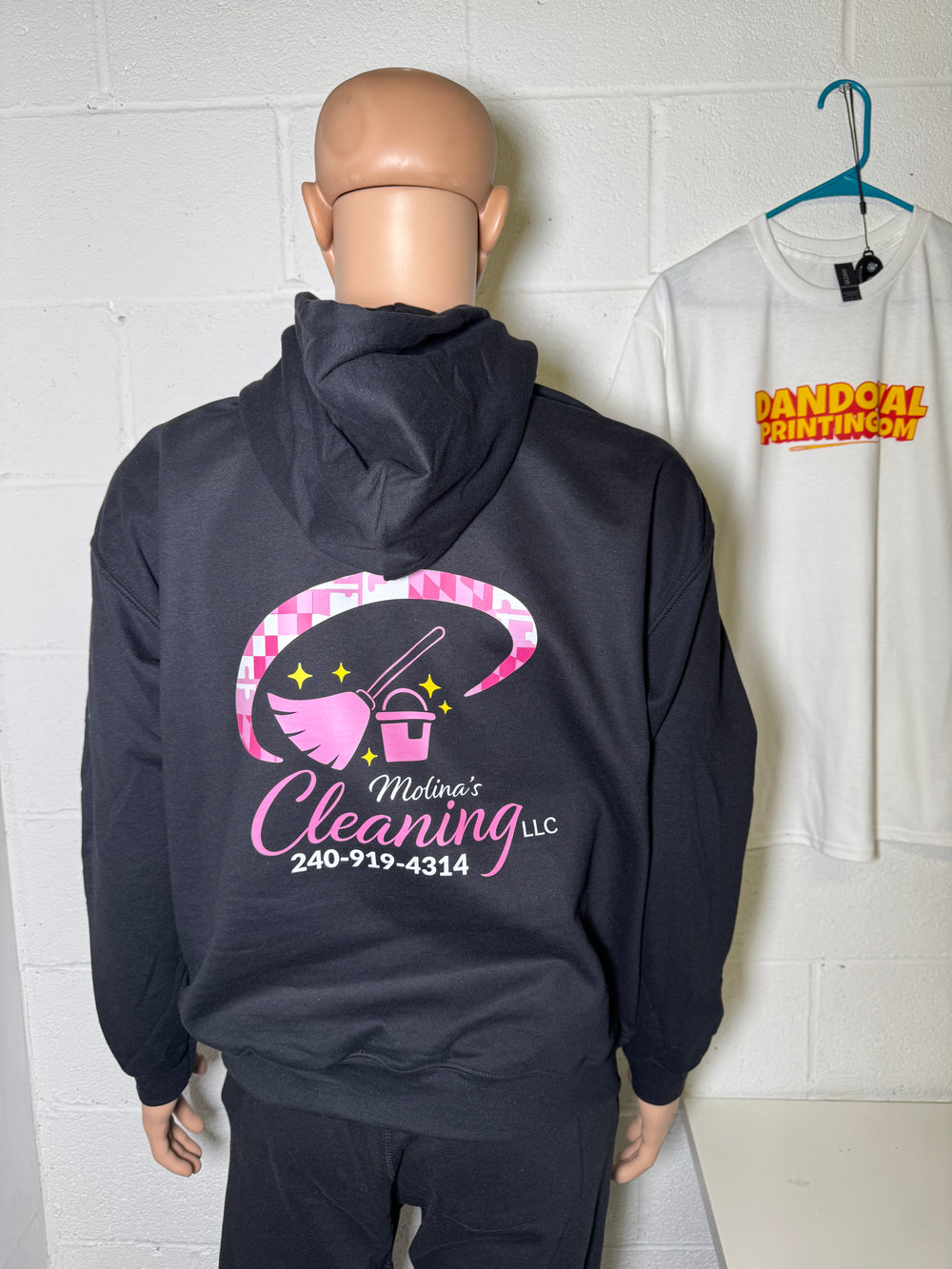 Person wearing a dark blue hoodie with a cleaning service logo on a tiled floor.