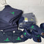 Stack of navy blue shirts and caps with green logos on a white surface against a tiled wall.