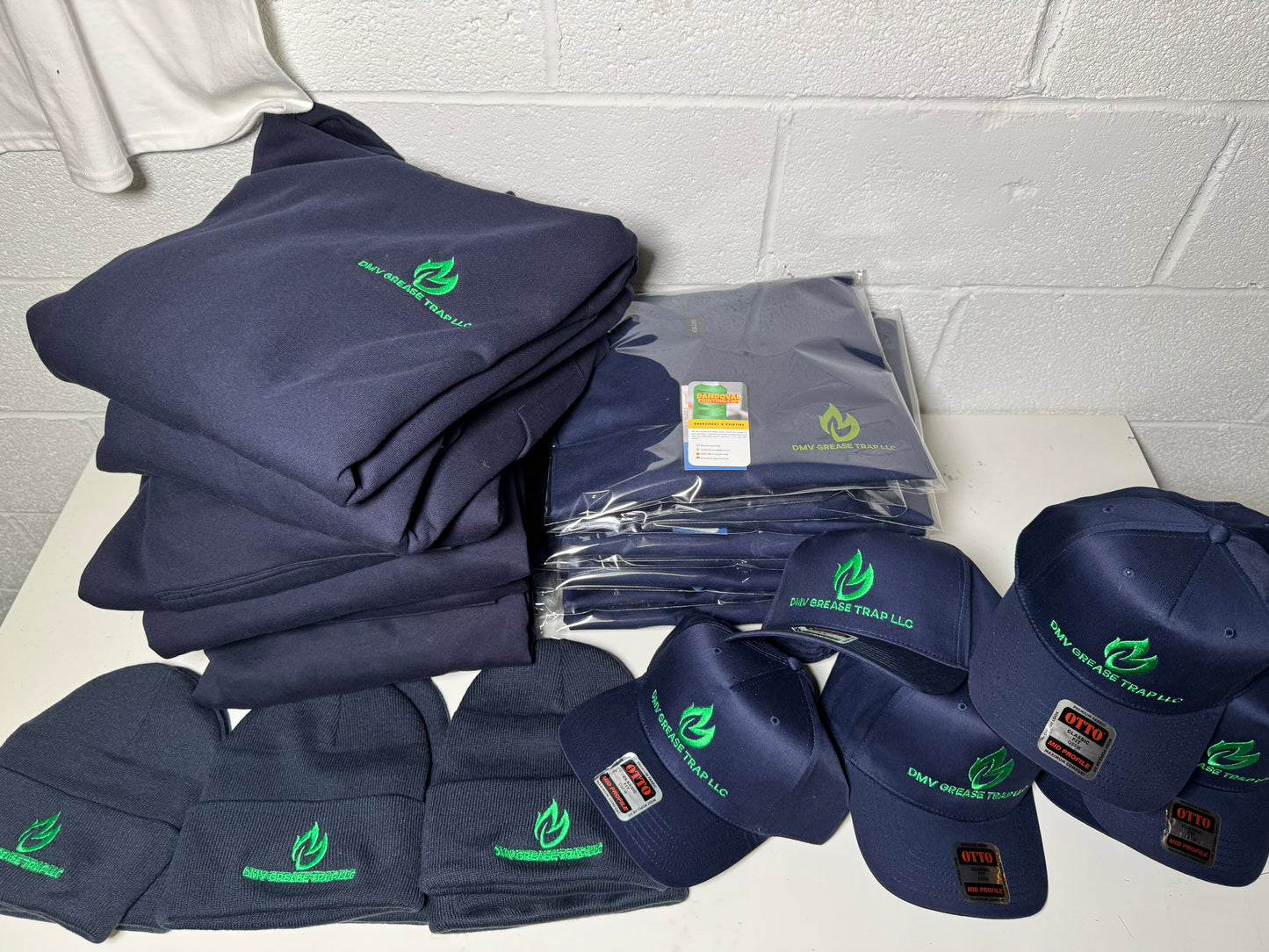 Stack of navy blue shirts and caps with green logos on a white surface against a tiled wall.