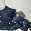 Stack of navy blue shirts, hats, and other items with logos on a white surface against a gray tiled wall.