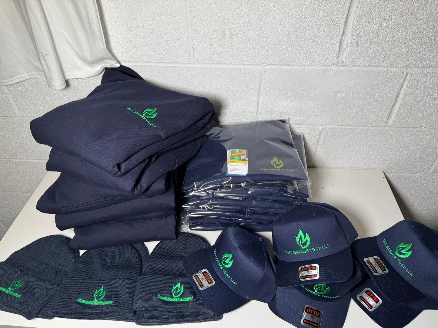 Stack of navy blue shirts, hats, and other items with logos on a white surface against a gray tiled wall.