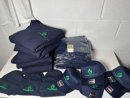 Stack of navy blue shirts, hats, and other items with logos on a white surface against a gray tiled wall.