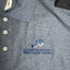 Gray shirt with embroidered logo and brand name on a neutral background