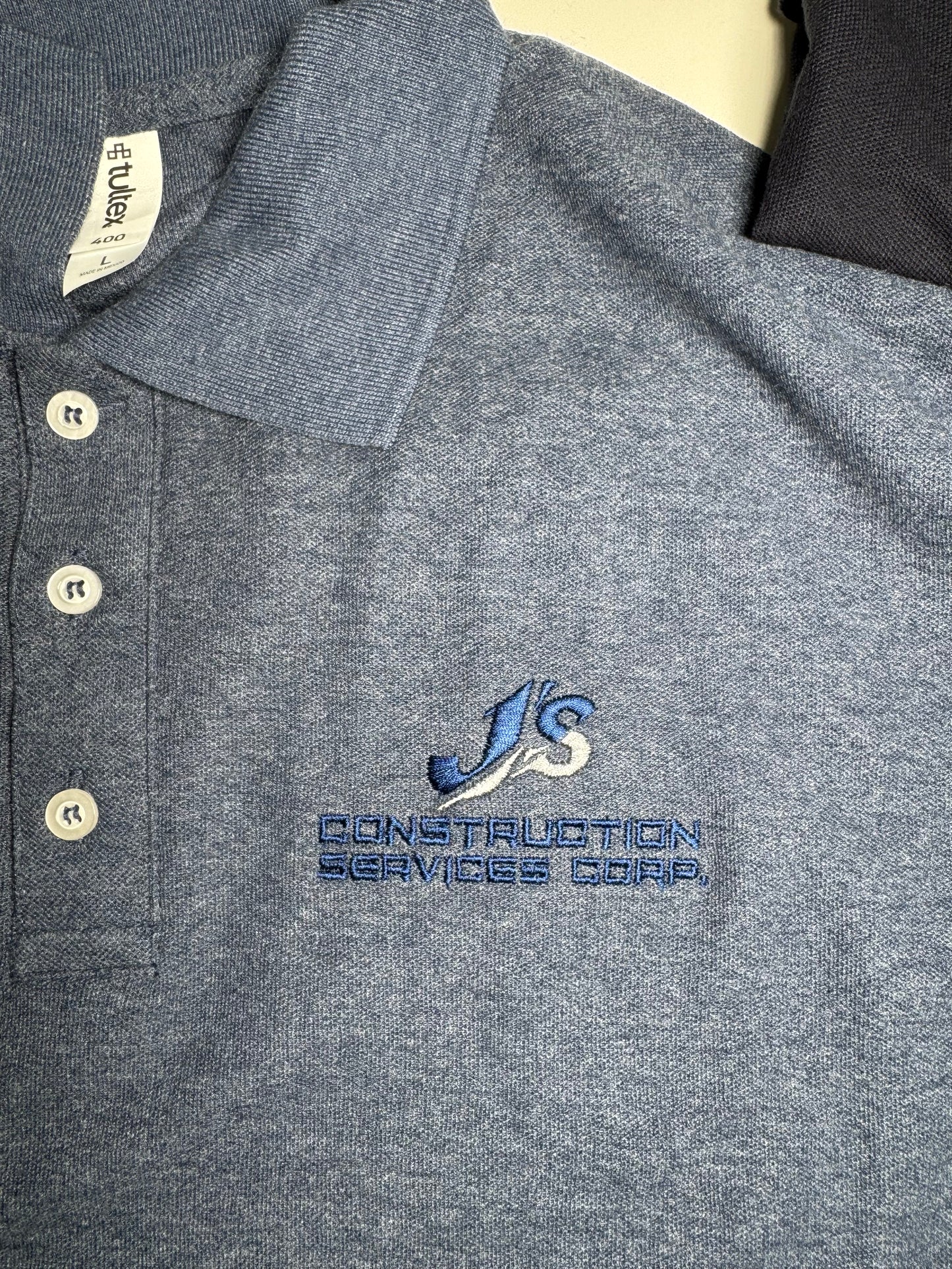 Gray shirt with embroidered logo and brand name on a neutral background