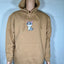 Beige hoodie with a cat graphic on a mannequin against a light gray brick wall.