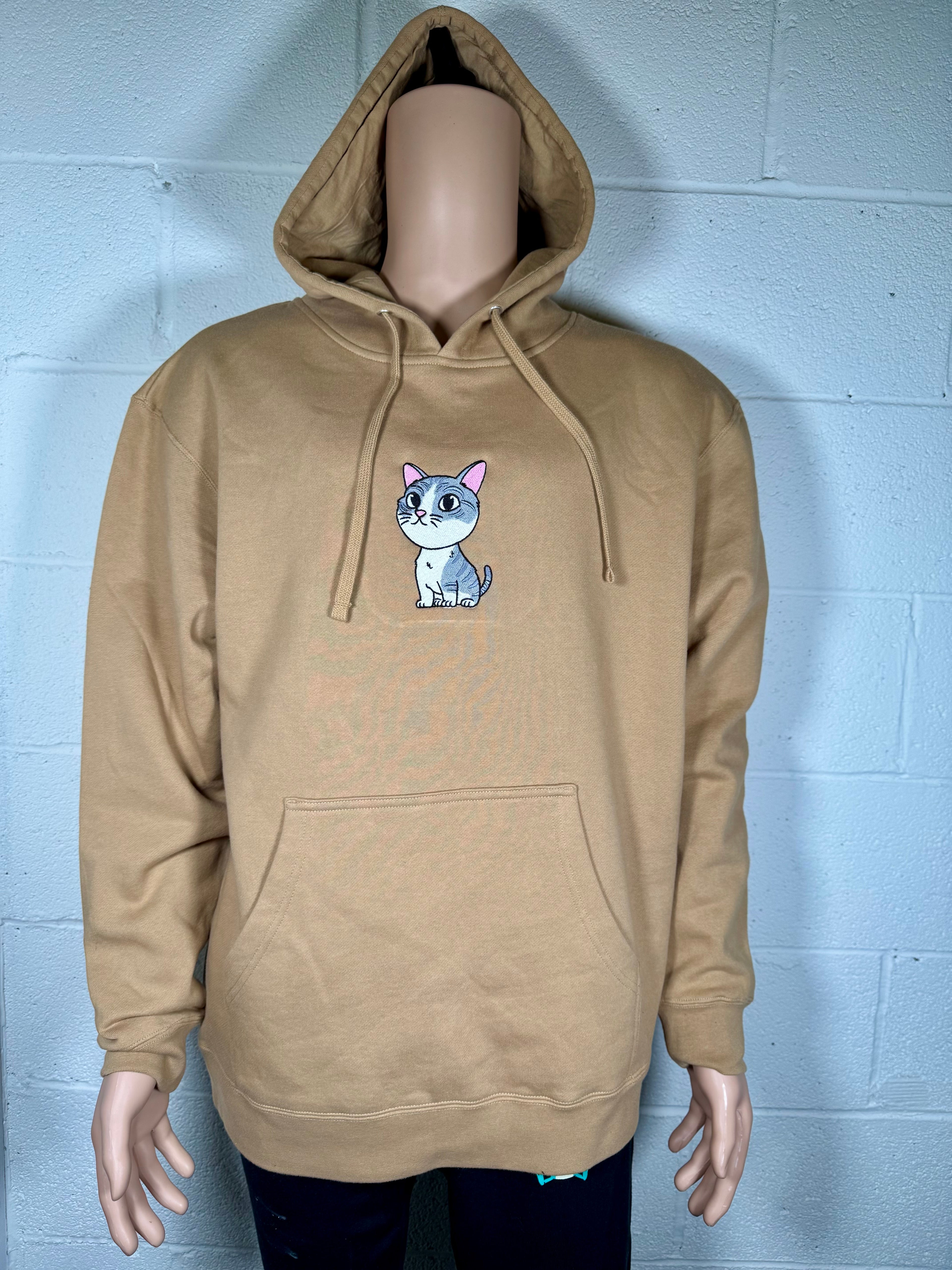 Beige hoodie with a cat graphic on a mannequin against a light gray brick wall.