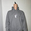 Gray hoodie with a small graphic on a mannequin against a tiled wall.