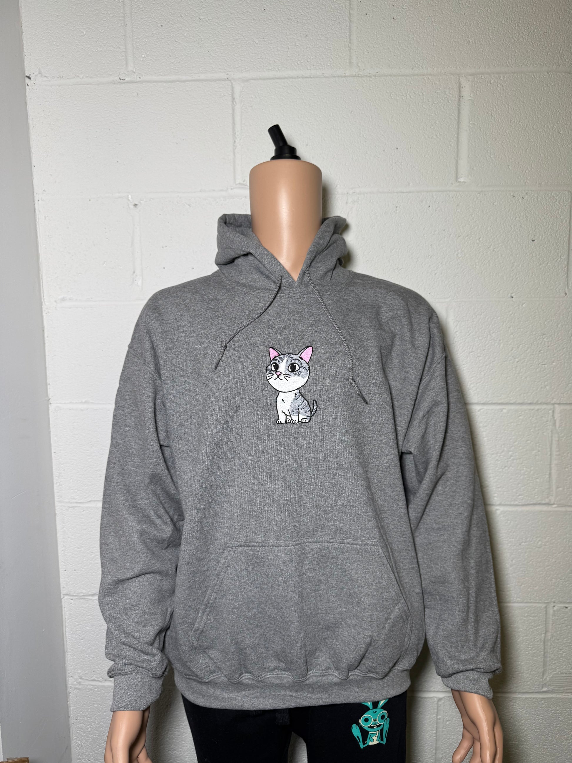 Gray hoodie with a small graphic on a mannequin against a tiled wall.