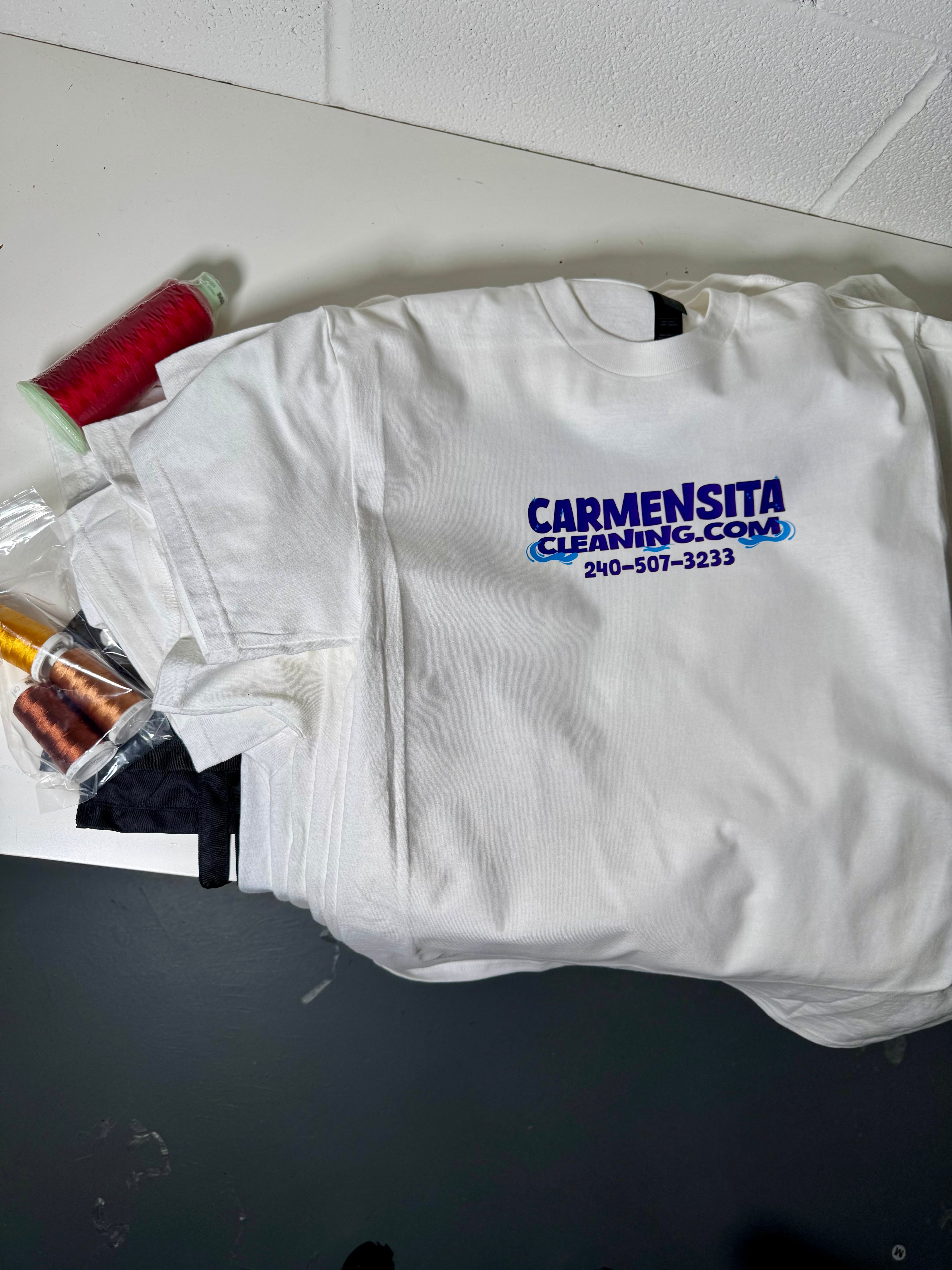 White shirt with 'Carmensita Cleaning' logo on a white surface.